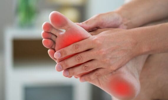 Person holding their foot with a red spot on it