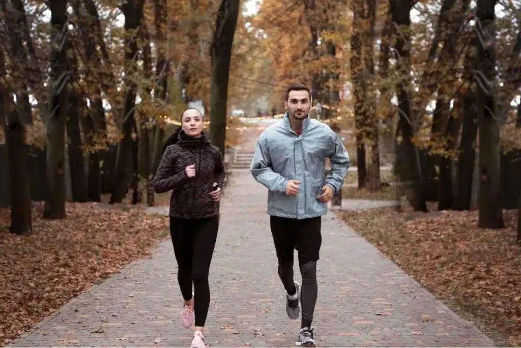 A man and a woman jogging together in a park during autumn.