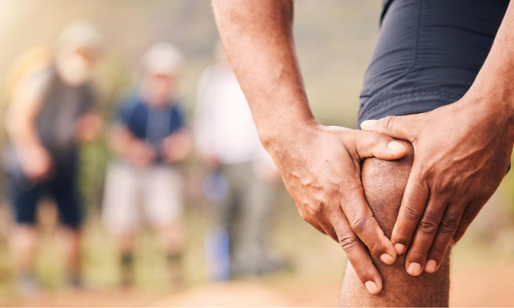 Person holding their knee in pain outdoors.