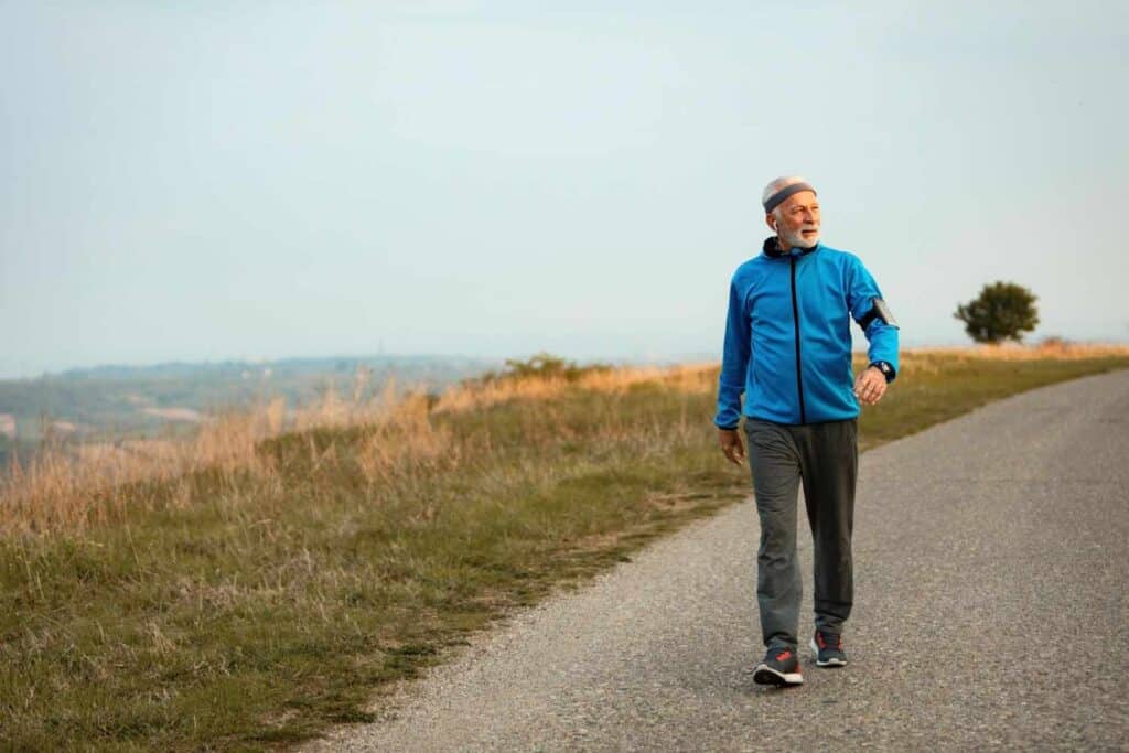 A senior man walking outdoors on a scenic path.