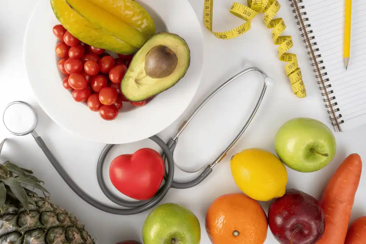 Healthy fruits, vegetables, a stethoscope, and a tape measure on a table.
